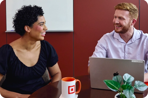 A female intern and male employee smiling as they discuss a topic