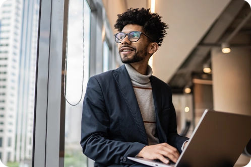 intern smiling as he sits by window working on his computer