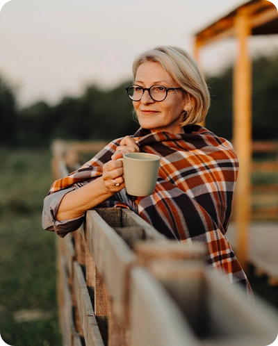 older woman sipping coffee outside her home while enjoying the sunrise