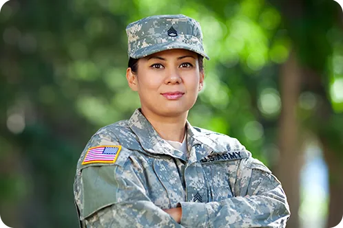 Woman dressed in U.S. Army uniform posing with arms crossed in front of greenery