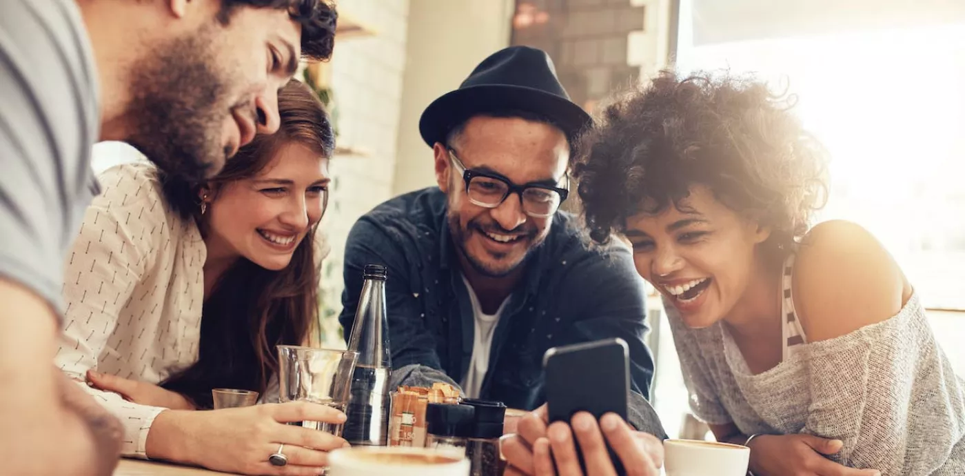 diverse group of young people smiling while using Zelle to send money at restaurant