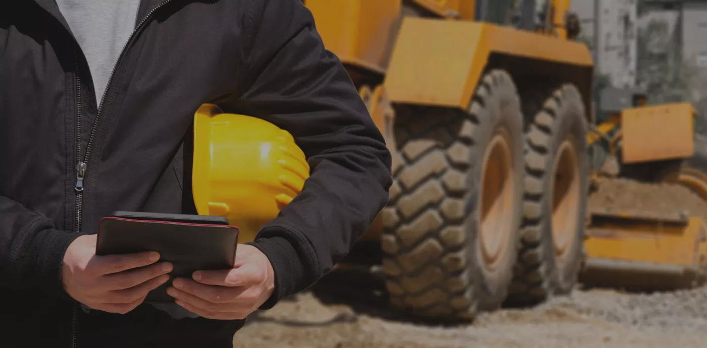 construction worker on tablet with construction equipment behind him