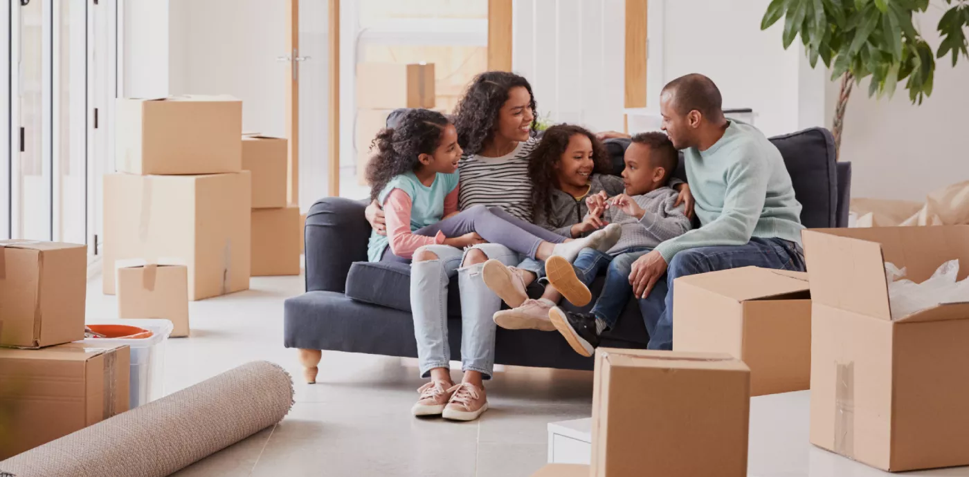 Family Taking A Break And Sitting On Sofa Celebrating Moving Into New Home Together