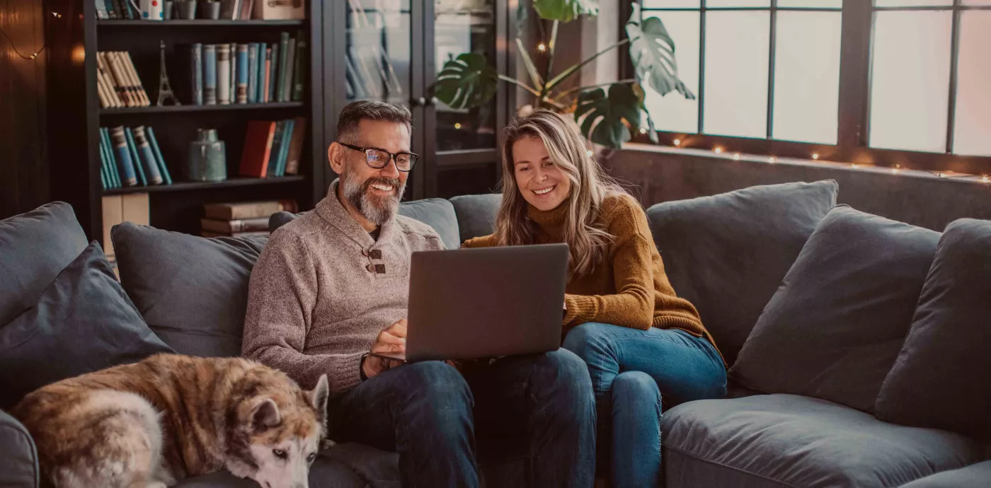 couple smiling while sitting on couch and looking at CD offers on computer screen