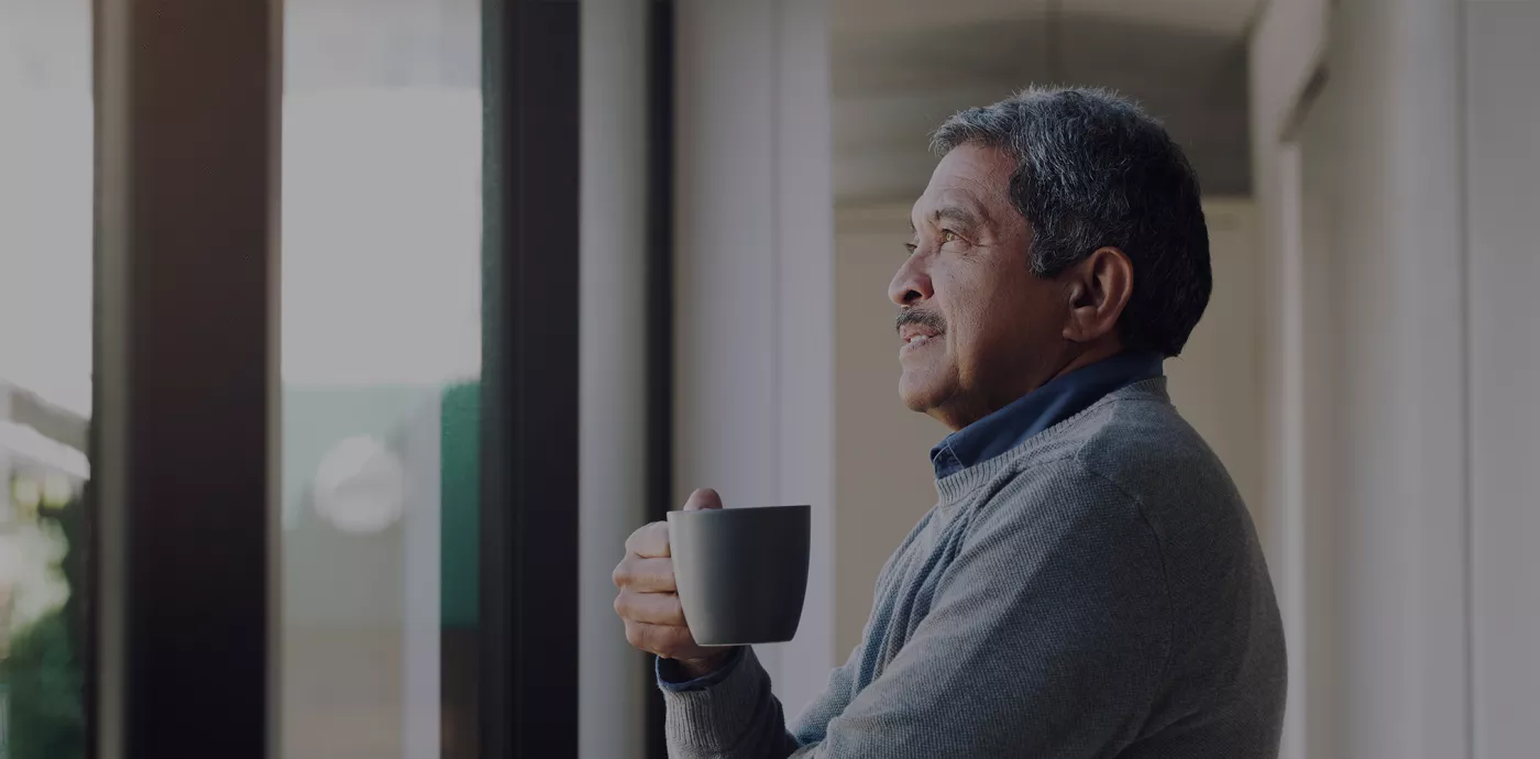 man smiling looking out the window while holding a cup of coffee