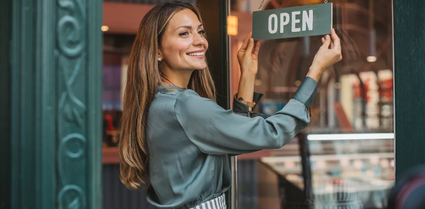 woman putting up open sign in front of her business