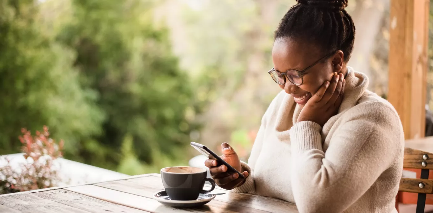 black woman using her phone and smiling while sitting in a cafe