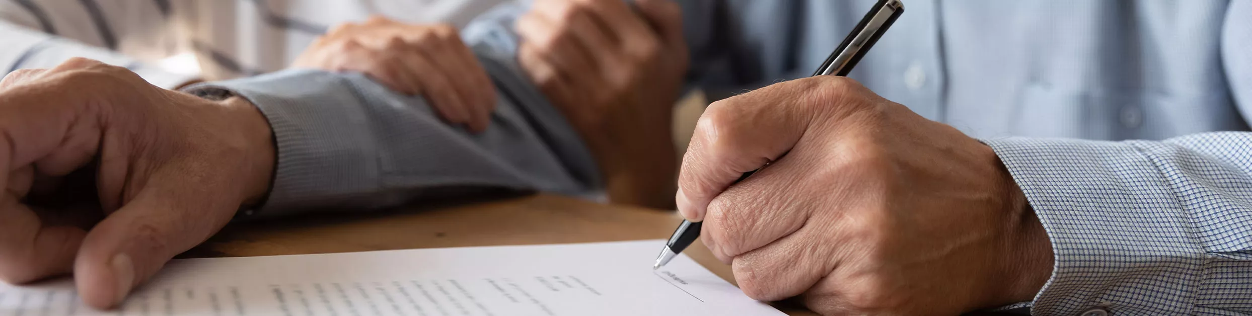an older woman's hands wrapped around and older man's arm while he signs a paper