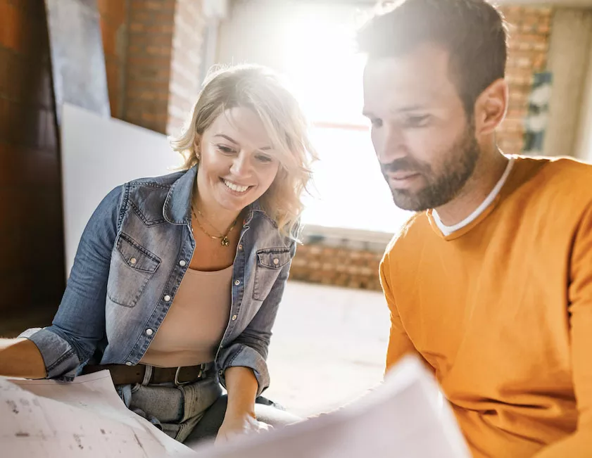 couple smiling while looking at building plans for their home